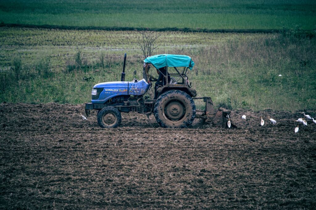 Blue tractor ploughing a field in India with white egrets following it