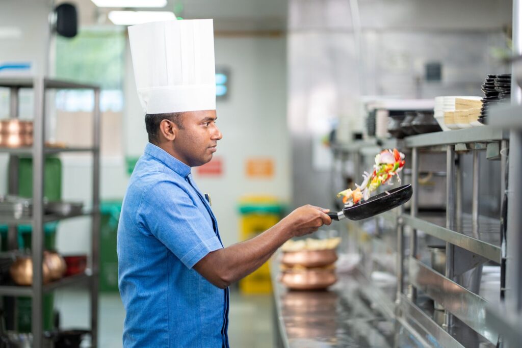 Chef tossing vegetables in a pan in a commercial kitchen